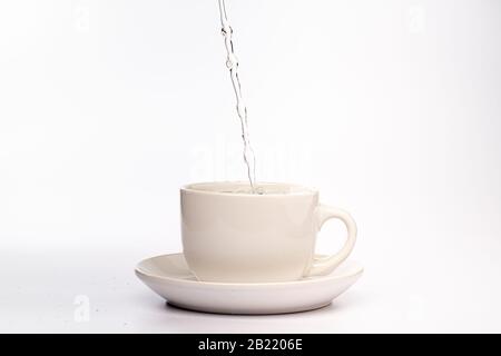 High Speed Studio Foto von Wasser gießen und spritzen in einen weißen Becher, isoliert vor einem einfarbigen weißen Hintergrund Stockfoto