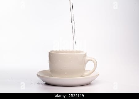 High Speed Studio Foto von Wasser gießen und spritzen in einen weißen Becher, isoliert vor einem einfarbigen weißen Hintergrund Stockfoto