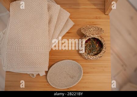 Natürliches, umweltfreundliches Badezubehör, Baumwolltücher, Seifenschale aus Stein und Korbkorb auf einer Holztischplatte Stockfoto