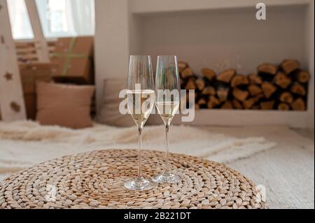 Zwei Perlmuttgläser mit Champagner, Blasen und Schaum, auf einem Korbtisch, vor dem Hintergrund eines hellen Innenraums mit Holzstämmen Stockfoto