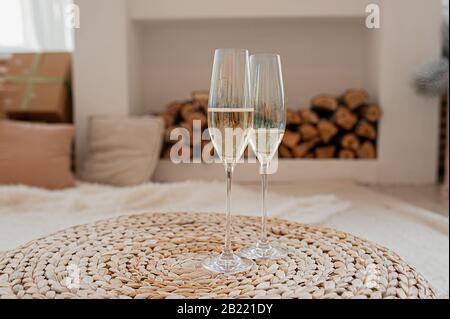 Zwei Perlmuttgläser mit Champagner, Blasen und Schaum, auf einem Korbtisch, vor dem Hintergrund eines hellen Innenraums mit Holzstämmen Stockfoto