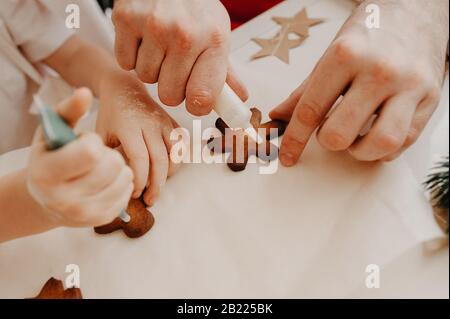 Die Hände von Mutter und Baby sind auf Plätzchen mit Lebensmittelfarbe auf Backpapier gemalt, auf einem weißen Tisch mit Dekor aus Papiersternen Stockfoto