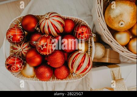 Riesiger Korbkorb, der oben mit roten und goldenen Kugeln gefüllt ist, um einen Weihnachtsbaum oder eine Wohnung zu schmücken Stockfoto