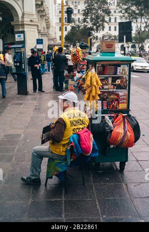 Lima, Peru - 16. Juli 2010: Money Changer and Vendor Sitting on the Sidewalk of a Street in Lima City, Peru, Holding a Sign. Stockfoto