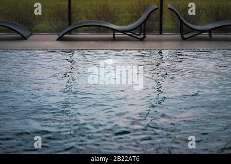 Blick auf das Wasser im Pool mit Fenstern und Sonnenliegen im Hotel Stockfoto