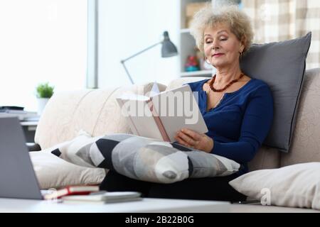 Ältere Frau sitzt zu Hause auf dem Sofa und liest Buch Stockfoto