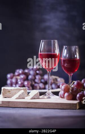 Ein Glas Rotwein. Nahaufnahme von Weinrebe und brie-käse auf dunkelblauem Hintergrund in niedriger Tonart. Kopierbereich. Banner für Café, Weingut. Stockfoto