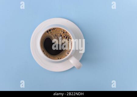 Draufsicht über Kaffee in Tasse mit Schaum auf blauem Hintergrund, schwarzer Kaffee mit Schaum auf dem Oberteil Stockfoto