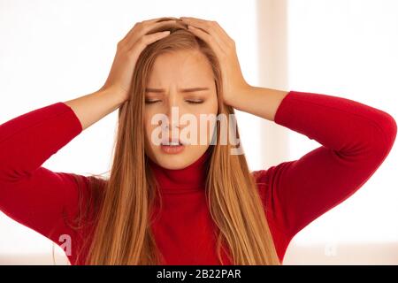 Junge blonde Frau mit ernstem Myren, die unter schrecklichen Kopfschmerzen leidet und schreckliche Schmerzen spürt. . Stockfoto