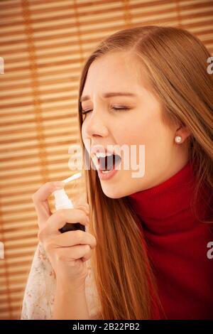 Auf Halsschmerzen sprühen. Foto einer Frau, die ihre Kehle mit einem Spray behandelt und sie in ihren Mund streut. Das Konzept der Gesundheit und Krankheit Stockfoto