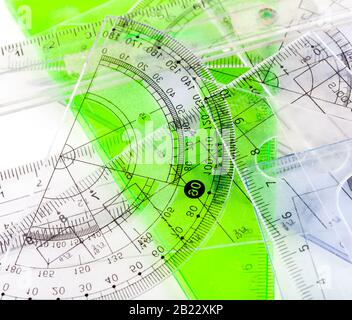 Viele gesetzte Quadrate, Lineale, ein Winkelmesser, verschiedene transparente Plastikschulartikel auf einem Tisch, Draufsicht, abstrakte Hintergrundtextur Stockfoto