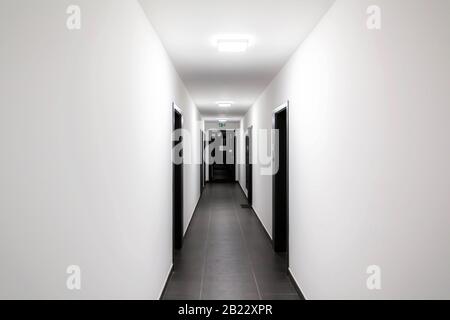 Einfach sauber, neu gebaut, generisch, modern, neuer Wohnblock innen, langer weißer Korridor mit schwarzen Türen, Perspektive. Neu gekaufte Wohnung Stockfoto