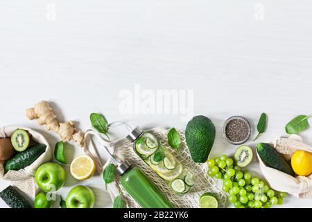Verschiedene grüne Obst- und Gemüsesorten mit Flaschen Smoothie und Wasser auf weißem Holztisch Draufsicht. Entgiftungsdiät. Umweltfreundliches Einkaufs-Konzept. Stockfoto