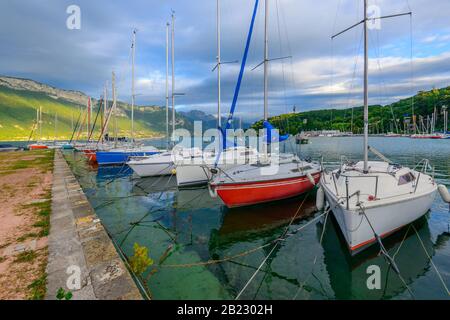 Segelboote, die auf dem See von Annecy, einem der größten Seen in Frankreich, der als sauberster See Europas bekannt ist, bei Sonnenuntergang festgemacht wurden. Stockfoto