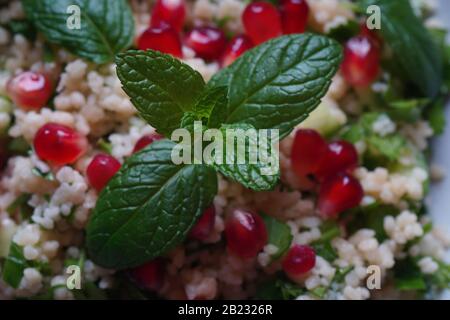 Gesunder Salat mit Couscous, frischer Minze, Gurke, Granatapfel, Zitrone und Olivenöl. Östliche Küche. Veganes Lebensmittelkonzept. Traditionelle israelische Küche Stockfoto