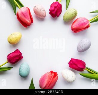 Dekorative ostereier und Tulpen im Kreis angeordnet. Weißer Hintergrund. Weihnachtsdekorationen, Hintergrund des Osterkonzepts. Draufsicht, flacher Lay. Stockfoto