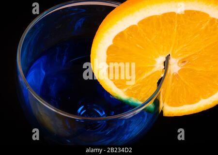 Oberseite des Glases mit blauem Getränk und Scheibe saftiger Orange auf der Seite Stockfoto