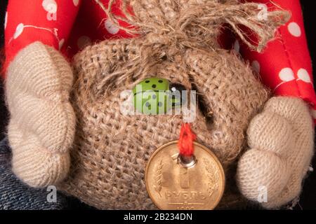 Hände aus weichem Spielzeug, die Leinwandtasche mit Geschenken, einen grünen Vogel und eine Münze für das Glück darauf halten Stockfoto