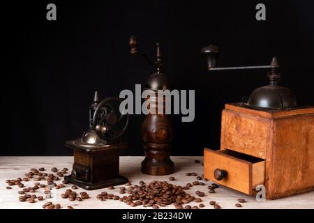 Manuelle Kaffeemühlen aus Holz und Pfeffermühle mit Kaffeebohnen, die auf einer Holzoberfläche verstreut sind Stockfoto