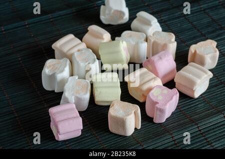 Mehrfarbige Marshmallows auf dunklem Hintergrund. Gruppe von Marshmallows auf einem Bambussubstrat. Nahaufnahme. Selektiver Fokus. Stockfoto