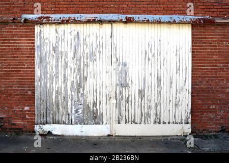 Hellweiß lackiert, aber Peeling-Lager Versand Doppeltüren auf rotem Backstein-Gebäude Stockfoto