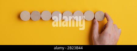 Weitsicht-Bild der männlichen Hand mit acht leeren Holzschnitten in einer Reihe über gelbem Hintergrund. Stockfoto