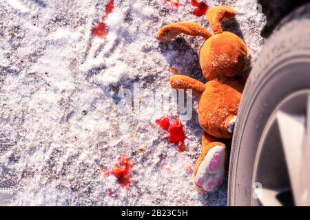 Kinderunfall auf einer Winterstraße, Hase Kaninchen Spielzeug. Tod auf der Straße, Unachtsamkeit und Gefahr. Achtung und Vorsicht. ROADKILL Winter, Blut an s. Stockfoto