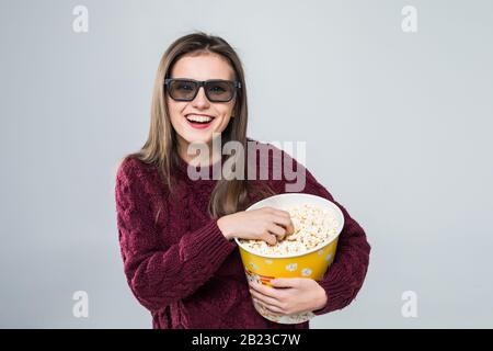 Mädchen in 3D-Brille trinkt Getränk mit einer Schale Popcorn und sieht Kino, isoliert auf Weiß Stockfoto