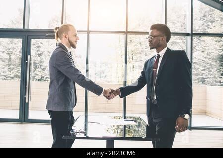 Der junge kaukasische Geschäftsmann schüttelt die Hände, um einen Deal mit seiner hübschen Frau zu schließen. Multiethnische Gruppe von Geschäftsleuten, die ein Unternehmen haben Stockfoto