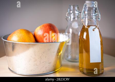 Nahansicht der Glasflasche mit apfelsaft und Äpfeln im Korb auf Holztisch Stockfoto