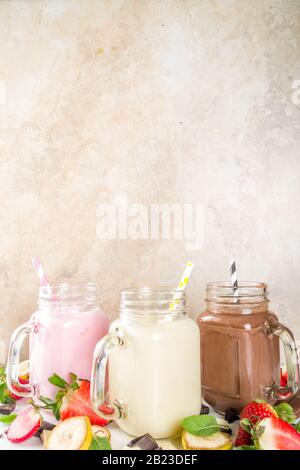 Drei Maurer-Gläser mit Milchshakes oder Smoothie. Sommer gesundes Frühstück, Mittagessen Getränke - Bananen, Schokolade und Erdbeermilchshakes auf Holzbackgroun Stockfoto