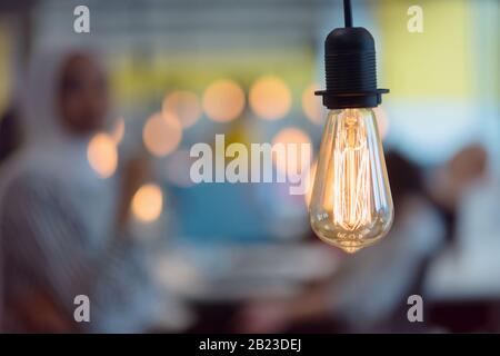 Nahaufnahme der modernen Glühbirne im modernen Inneren des Unternehmens in Unschärfe mit den Arbeitgebern. Stockfoto