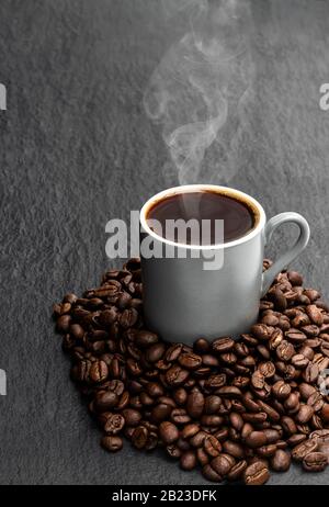Schwarzer Kaffee in kleiner Tasse mit Bohnen auf schwarzem Steingrund Stockfoto