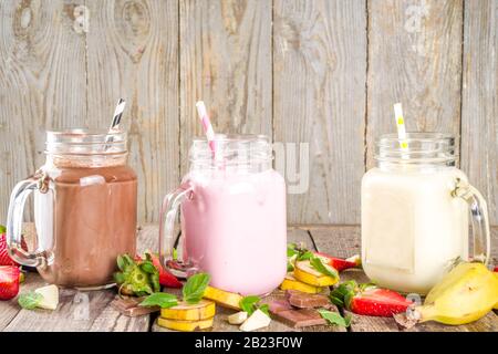 Drei Maurer-Gläser mit Milchshakes oder Smoothie. Sommer gesundes Frühstück, Mittagessen Getränke - Bananen, Schokolade und Erdbeermilchshakes auf Holzbackgroun Stockfoto