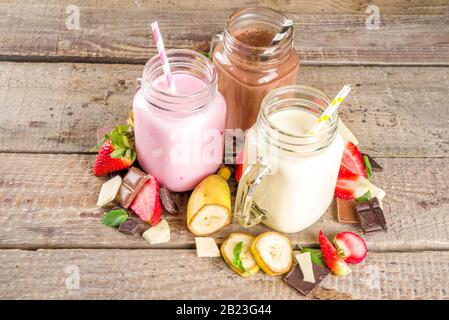 Drei Maurer-Gläser mit Milchshakes oder Smoothie. Sommer gesundes Frühstück, Mittagessen Getränke - Bananen, Schokolade und Erdbeermilchshakes auf Holzbackgroun Stockfoto