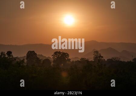 Silhouetten von Bäumen und geschichteten Bergen in orangefarbenem Licht mit untergehenden Sonne im Hintergrund in der thailändischen Region Khao Yai Stockfoto