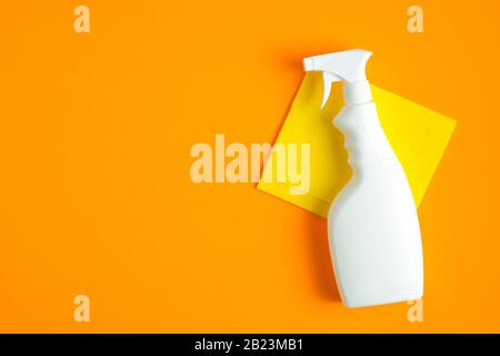 Leere Reinigungs-Sprühflasche und gelber Lappen auf orangefarbenem Hintergrund. Flache Lage, Draufsicht. Haustreinigungsservice und Hauswirtschaftskonzept. Stockfoto