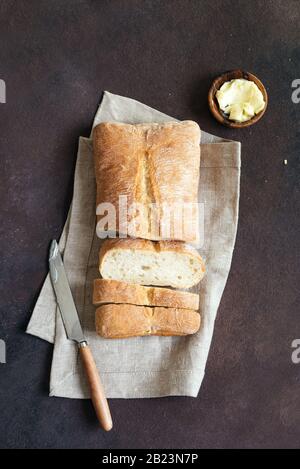 Brot und Butter auf dunklem Tisch, Kopierraum. Frisches Ciabatta Brot und Biobutter zum Frühstück. Stockfoto