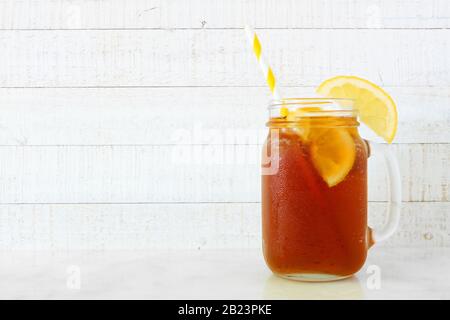Sommerlicher Eistee in einem Maurerglas. Seitenansicht auf weißem Holzhintergrund. Stockfoto