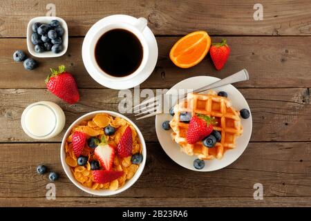 Frühstücksszene. Obst, Müsli und Cornflakes, Waffeln, Milch und Kaffee. Draufsicht über einen dunklen Holzhintergrund. Stockfoto