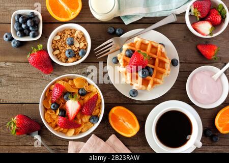Frühstücksszene. Obst, Müsli und Cornflakes, Waffeln, Joghurt und Kaffee. Draufsicht über einen dunklen Holzhintergrund. Stockfoto