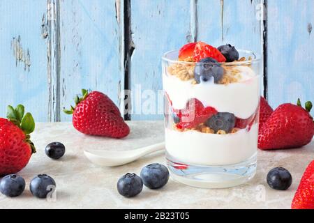 Erdbeere und Blaubeere parfait in einem Glas vor einem rustikalen blauen Holzhintergrund Stockfoto