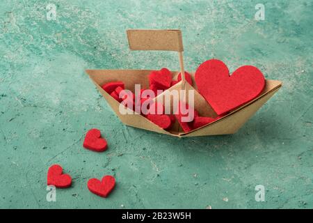 Handgefertigtes Segelboot aus Papier auf aquamarinem Hintergrund, Origami Papierboot mit roten Herzen dekoriert Stockfoto