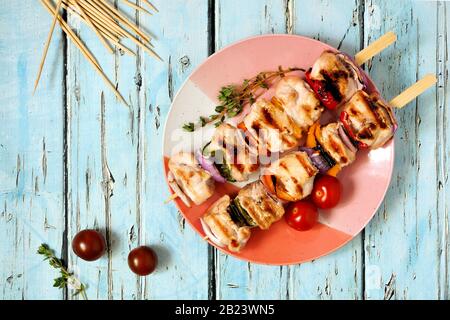 Gegrilltes Huhn und Gemüsekabobs auf dem Teller. Draufsicht über einen blauen Holzhintergrund. Sommernahrungskonzept. Stockfoto