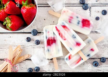 Gesunde Erdbeerjoghurt Popsicles, Top View Sommertisch-Szene mit weißem Holzhintergrund Stockfoto