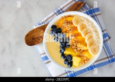 Gesunde Ananas, Mango-Smoothie-Schüssel mit Kokosnuss, Bananen, Blaubeeren und Granola. Draufsicht auf hellem Hintergrund. Stockfoto