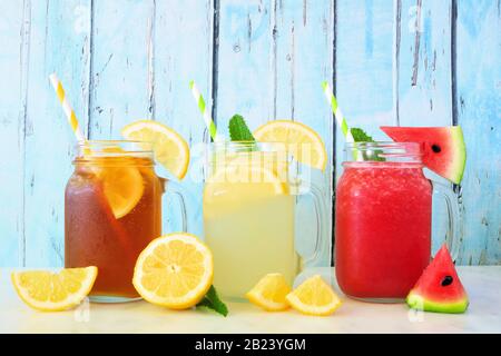 Verschiedene Sommergetränke in Maurergläsern mit Obst vor blauem Holzhintergrund. Eistee, Limonade und Wassersaft. Stockfoto