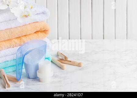 Blaues Kunststoff-Messgefäß mit Waschpulver, Behälter mit Waschmittel, mehrfarbige Frottiertücher, Holzkleiderinnen und weiße Orchidee Stockfoto