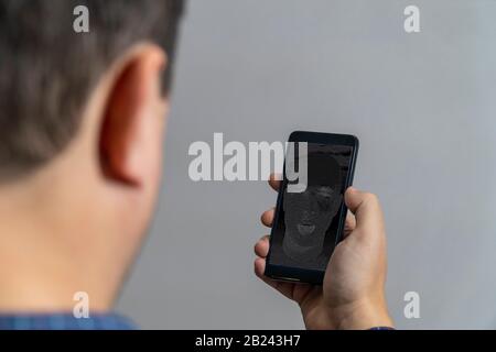 AI bot Konzept. Eine Person, die einen Smartphone-Bildschirm mit KI-Gesicht darauf betrachtet. Stockfoto