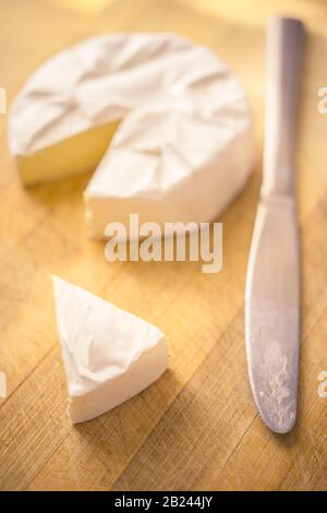 Camembert-Käse mit einer Dreiecksscheibe und einem Messer auf einem Holzbrett Stockfoto